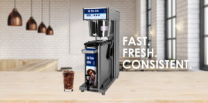 Cold Brew Brewer sitting on top of a butcher block counter in a restaurant environment. Has the tag line, "Fast.Fresh.Consitent" counter